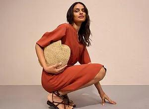 Rostfarbenes Jumpsuit mit kurzen Ärmeln, ergänzt durch eine Strohhandtasche und zierliche Sandalen.